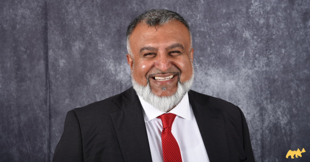 The Summit Chauffeur's main man and executive chauffeur, Rehan Jamil, smiling at the camera, wearing a black suit, white shirt and red tie.